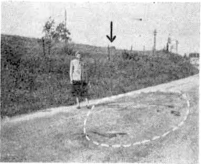 Près de notre secrétaire générale, et entourê d'un pointillé blanc : l'ensemble des taches épaisses        relevées sur la route à l'endroit-même de l'observation et aussitôt après. Ces taches, encore molles,        n'existaient pas auparavant. Elles durcirent par la suite. L'une d'elles portait encore l'empreinte toute        fraîche d'un pneu de l'automobile qui était passée pendant l'observation. - À droite : le transformateur. - La        flèche indique la ferme de M. Chatelain dans le lointain. On comprend, par le rapprochement panoramique de        cette photo et de celle de gauche, qu'il était absolument impossible de confondre une lampe-tempête tenue par        une personne gravissant lu butte en direction de la ferme Chatelain et une lumière s'élançant dans le ciel à 45        degrés s3Clichés Ouranos