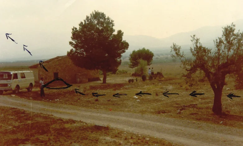 Countryside with a small house, a pine tree and a van, with black arrows drawn along the ground from the right to a curved mark near the house