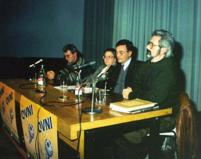 Four people seated behind a table with microphones, posters reading OVNI hanging from its front